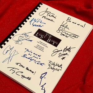 Könnte beinhalten: Ein weißes Drehbuch für den Film "The Lost Boys" mit Unterschriften der Darsteller, darunter Corey Feldman, Jamison Newlander, Jason Patric, Kiefer Sutherland und andere. Das Drehbuch liegt auf einem roten Hintergrund.