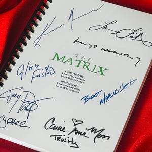 May include: A white page with the title "The Matrix" and signatures from the cast and crew. The signatures include "Carrie-Anne Moss Trinity", "Hugo Weaving", "Lilly Wachowski", "Lana Wachowski", "Joe Pantoliano", "Gloria Foster", "Marcus Chong", "Jada Pinkett Smith", and "Keanu Reeves".