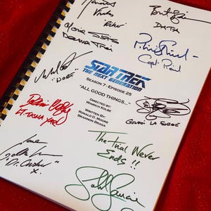 Puede incluir: Un guion encuadernado en espiral de Star Trek: The Next Generation, Temporada 7, Episodio 25, titulado "All Good Things...". Las páginas blancas están cubiertas de firmas coloridas. El guion está sobre una superficie roja.