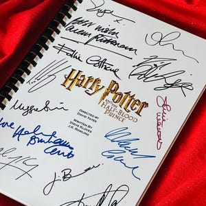 Puede incluir: Un cuaderno blanco con encuadernación en espiral, con el título "Harry Potter y el Príncipe Mestizo". El cuaderno está firmado por varias personas, incluido el director, el guionista y miembros del reparto.