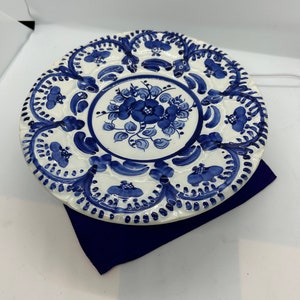 May include: A white ceramic plate with a blue floral design. The plate has a scalloped edge and is decorated with intricate blue patterns.