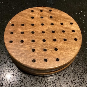 Peut inclure: Un jeu de société en bois rond, de couleur marron foncé. Le plateau comporte de nombreux trous espacés régulièrement. Le diamètre du plateau est d'environ 15 cm.