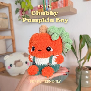 Puede incluir: Un peluche con forma de calabaza con cuerpo naranja brillante, tallo marrón claro y hojas verdes rizadas. El juguete lleva un peto blanco y verde oscuro con botones pequeños. Tiene ojos negros de seguridad y una sonrisa bordada en la cara.