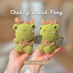 Könnte beinhalten: Zwei grüne gehäkelte Frosch-Plüschtiere mit braunen Geweihen und Blättern. Die Frösche haben rosa Wangen und sind mit einem hellbraunen Band gebunden. Der Text auf dem Bild lautet "Low Sew" und "Chubby Druid Frog". Der untere Teil des Bildes lautet "PDF PATTERN ONLY".