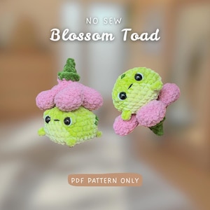 Könnte beinhalten: Zwei gehäkelte Plüschkröten mit weichen, flauschigen hellgrünen Körpern und rosa blütenartigen Kappen. Der Text NO SEW Blossom Toad und PDF PATTERN ONLY ist sichtbar. Die Kröten haben große schwarze Sicherheitsaugen und kleine Münder.