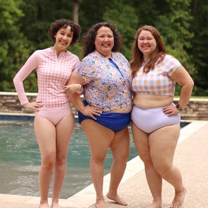 Puede incluir: Tres personas con trajes de baño de pie cerca de una piscina. Los trajes de baño incluyen un protector contra erupciones a cuadros rosa y blanco y una parte inferior, una parte superior con estampado floral con una parte inferior azul y una parte superior corta a cuadros con una parte inferior lavanda.
