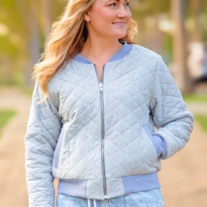 Könnte beinhalten: Eine graue gesteppte Bomberjacke mit Reißverschluss und blauem geripptem Kragen und Bündchen. Die Jacke hat ein Rautenmuster und einen Kordelzug in der Taille.