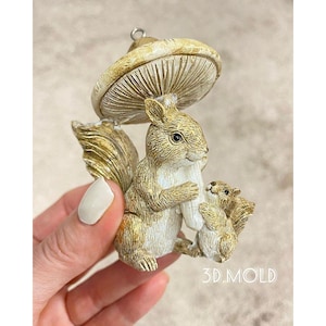 May include: A ceramic squirrel figurine with a mushroom cap on its head. The squirrel is holding a smaller squirrel figurine in its arms. The figurines are painted in shades of brown and white.