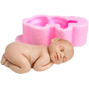 Puede incluir: Una figura realista de un bebé durmiendo junto a un molde de silicona rosa. El bebé tiene los ojos cerrados y una boca pequeña. El molde tiene forma de bebé. Fondo blanco.
