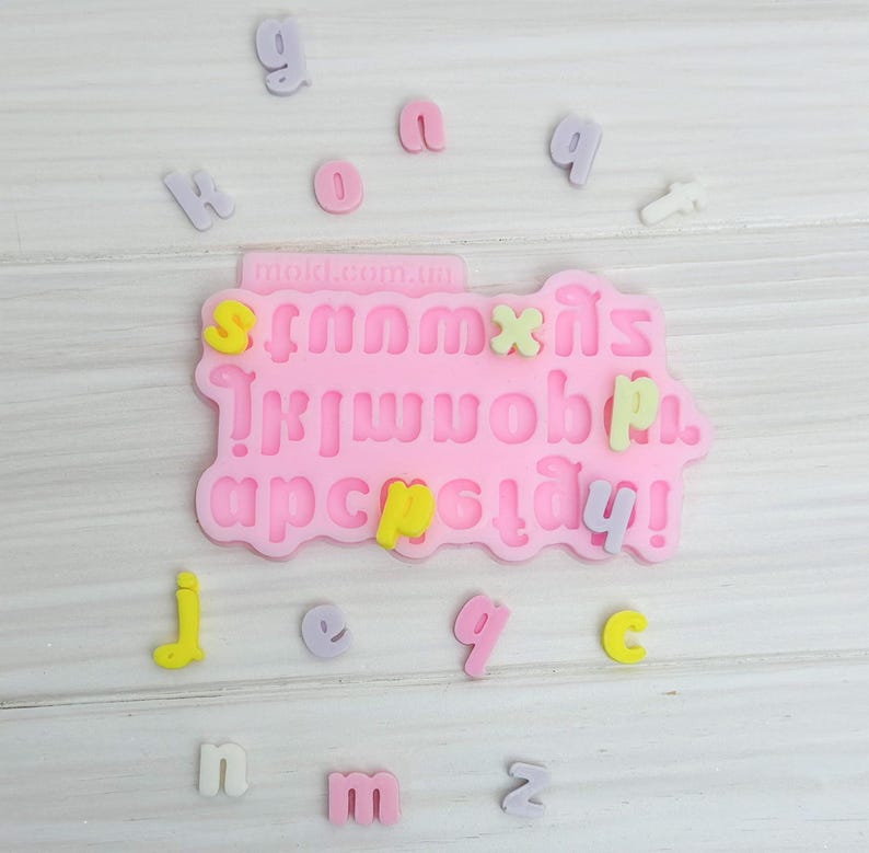 Puede incluir: Molde de silicona rosa con letras del alfabeto, n&uacute;meros y signos de puntuaci&oacute;n. El molde est&aacute; rodeado de peque&ntilde;as letras y n&uacute;meros de colores.