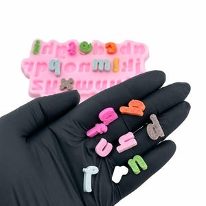 Puede incluir: Primer plano de una mano sosteniendo letras del alfabeto de colores. Las letras est&aacute;n hechas de un material suave y texturizado y son perfectas para manualidades o decoraci&oacute;n.
