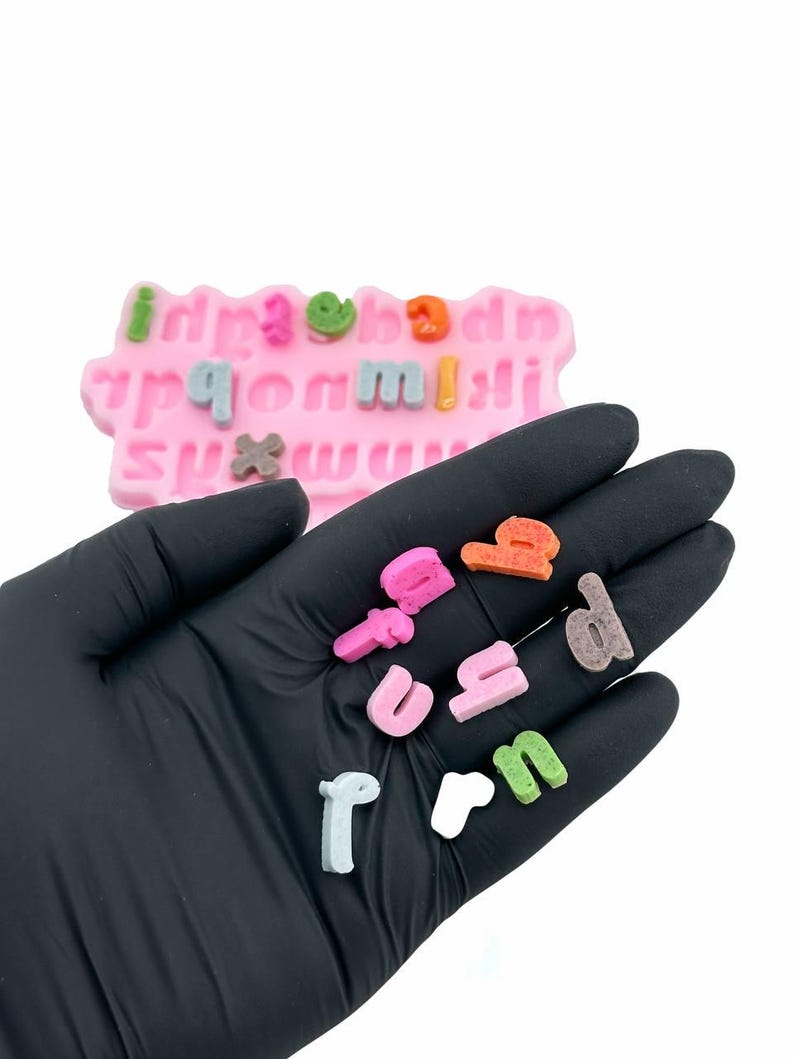 Puede incluir: Primer plano de una mano sosteniendo letras del alfabeto de colores. Las letras est&aacute;n hechas de un material suave y texturizado y son perfectas para manualidades o decoraci&oacute;n.