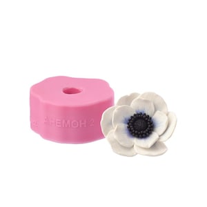 Könnte beinhalten: Rosa Silikonform zum Herstellen einer weißen Anemone mit blauem und schwarzem Zentrum. Die Form trägt den Text "AHEMOH 2" an der Seite.
