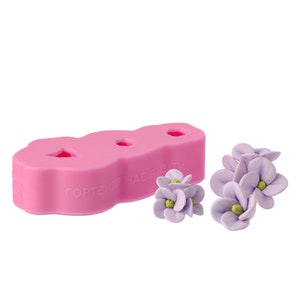 Puede incluir: Molde de silicona rosa con tres cavidades con forma de flores de hortensia. El molde tiene el texto "Гортензия набор" en ruso. También hay tres flores de hortensia moradas hechas de fondant.