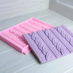 May include: Two silicone moulds for baking, one pink and one purple, with a cable knit pattern.