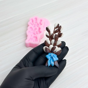 May include: A hand holding a handmade polymer clay bouquet of white and brown pussy willow branches tied with a blue ribbon. The bouquet is made to look like a real pussy willow bouquet.