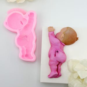 May include: Pink silicone mould of a baby in a pink onesie, with a matching pink fondant baby in a pink onesie.