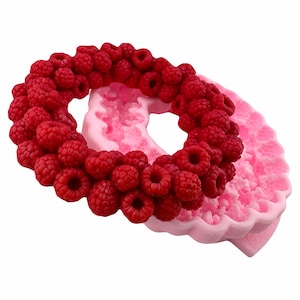 Puede incluir: Molde de silicona rosa en forma de corona con un anillo de frambuesas rojas alrededor del exterior.