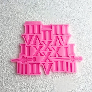 Può includere: Stampo in silicone rosa con numeri romani I, II, III, IV, V, VI, VII, VIII, IX, X, XI, XII. Lo stampo è progettato per creare elementi decorativi per l'artigianato o la cottura.