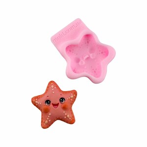 Peut inclure: Moule en silicone rose pour faire un topper de gâteau en forme d'étoile de mer. Le moule présente une étoile de mer souriante avec un design détaillé. Le moule est étiqueté "mold.com.au".
