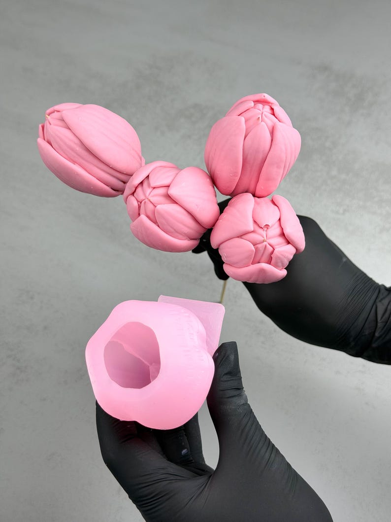 Pu&ograve; includere: Stampo in silicone a forma di tulipano rosa e un bouquet di boccioli di tulipano rosa. Lo stampo &egrave; tenuto da una persona con guanti neri. I boccioli di tulipano sono su uno stelo di legno. Lo sfondo &egrave; di colore grigio chiaro.