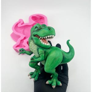 Peut inclure: Figurines de dinosaure vert avec un sourire narquois, debout sur une surface noire. Le dinosaure a une peau texturée et écailleuse et est posé dans une position dynamique.