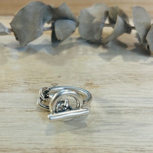 Peut inclure: Une bague en argent avec un design unique comprenant un cercle et une barre. La bague est en métal et a une finition polie.
