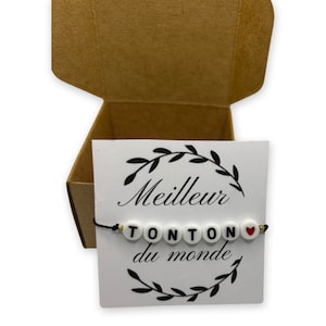 May include: A white card with black text that reads "Meilleur Tonton du monde" with a black string bracelet with white beads that spell out "Tonton" and a red heart bead. The bracelet is in a small brown cardboard box.