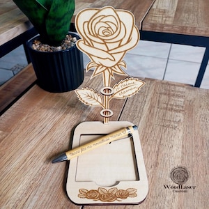 Puede incluir: Organizador de escritorio de madera con forma de rosa con un bloc de notas y un portaplumas. La rosa tiene el texto "Je t'aime Maman" grabado. El bloc de notas tiene el texto "Bonne fête ma merveilleuse Maman" grabado.