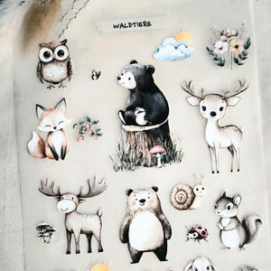 May include: A sheet of woodland animal stickers featuring an owl, fox, bear, deer, moose, raccoon, squirrel, bunny, hedgehog, and other forest creatures. The stickers are in a watercolor style with soft colours.