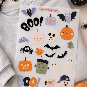 Könnte beinhalten: Ein transparenter Aufkleberbogen mit verschiedenen Halloween-Motiven wie Kürbissen, Geistern, Fledermäusen, Spinnen, einem Totenkopf und einem Frankenstein-Monster. Der Bogen enthält den Text HALLOWEEN ROSA, BOO!, Boo! sowie die URL www.oh-hallo-designs.de.