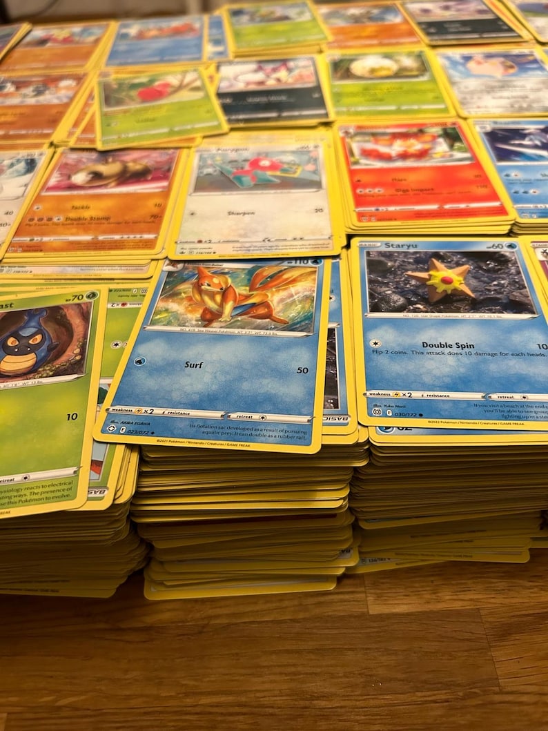 May include: A selection of Pok&eacute;mon trading cards, showcasing diverse characters and artwork. The cards are arranged in stacks and spread out, with yellow borders and vibrant illustrations. Some cards display text such as "Surf" and "Double Spin".