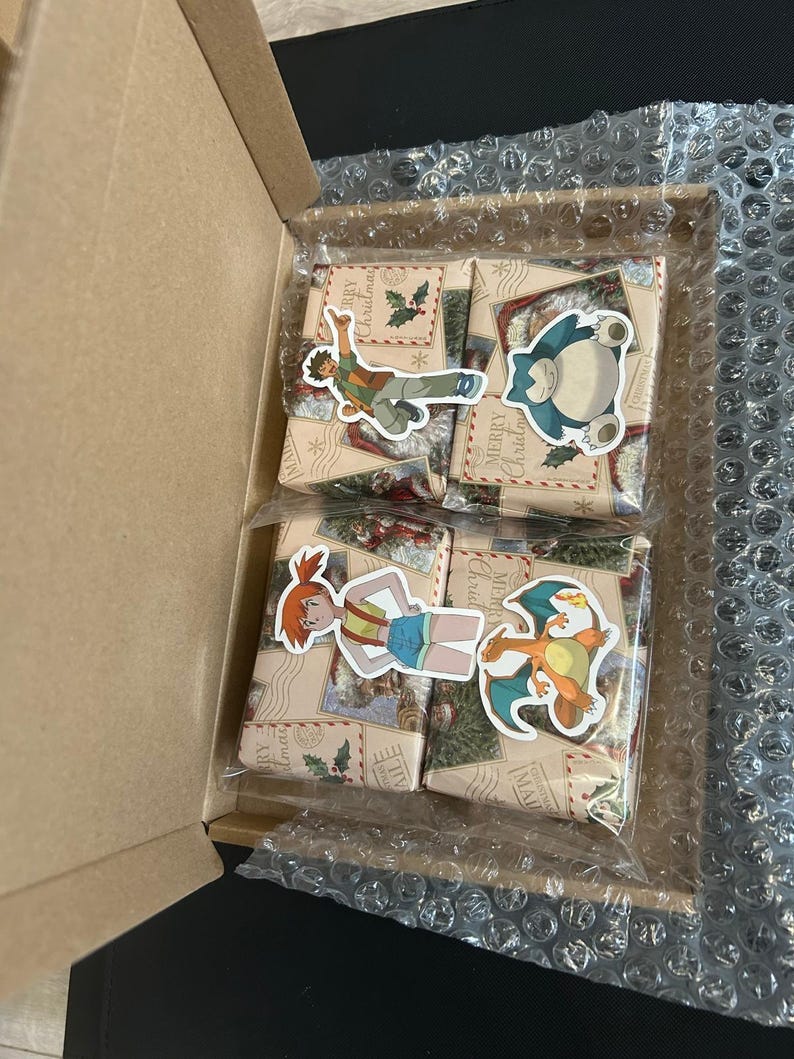 May include: A cardboard box containing four wrapped gifts. Each gift is wrapped in patterned paper and sealed with a clear plastic bag. Stickers of cartoon characters are on the gifts. The box is lined with bubble wrap.