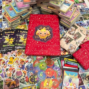 May include: A selection of Pok&eacute;mon trading cards, stickers, and merchandise. The image shows stacks of cards, a red binder with a Pok&eacute;mon design, and card packs. The items are displayed on a surface covered with Pok&eacute;mon artwork.