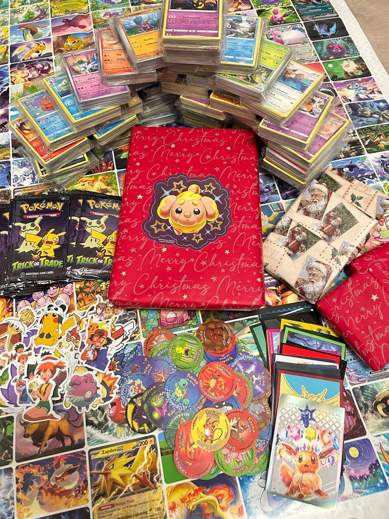 May include: A selection of Pok&eacute;mon trading cards, stickers, and merchandise. The image shows stacks of cards, a red binder with a Pok&eacute;mon design, and card packs. The items are displayed on a surface covered with Pok&eacute;mon artwork.