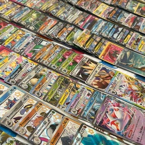 May include: A selection of vibrant trading cards, displaying diverse characters and designs. The cards are organised in rows, highlighting a range of artwork and text. The cards seem to be in protective sleeves, focusing on collectible card games.