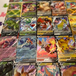 May include: A selection of Pok&eacute;mon trading cards, showcasing diverse characters and vibrant designs. The cards display character names, attack details, and numerical values. The cards are arranged on a light-coloured surface.