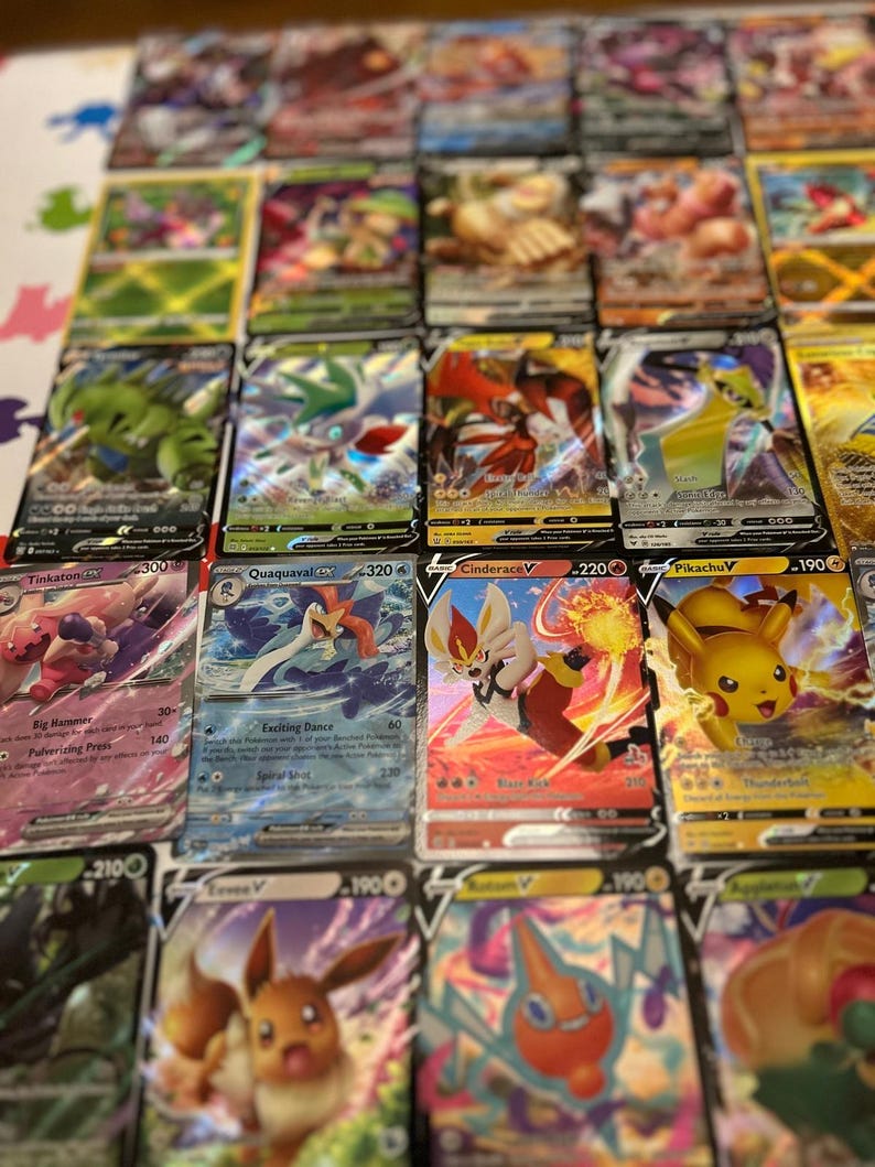 May include: A selection of Pok&eacute;mon trading cards, showcasing diverse characters and vibrant designs. The cards display character names, attack details, and numerical values. The cards are arranged on a light-coloured surface.