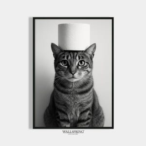 May include: Black and white framed print featuring a tabby cat with a roll of toilet paper balanced on its head. The cat is centered, looking directly at the viewer. The print has a minimalist aesthetic and includes the text "WALLSPRING art for your walls".