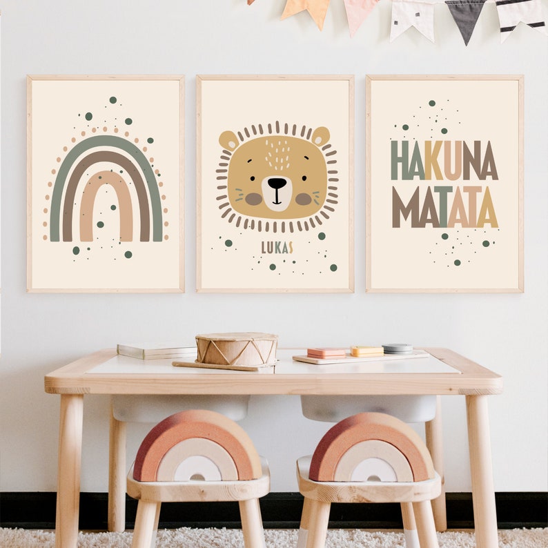 May include: Three framed prints with a boho nursery theme. The left print features a rainbow with brown, orange, and green colors. The middle print features a lion's face with the name "Lukas" below. The right print features the phrase "Hakuna Matata" in brown, orange, and green colors.