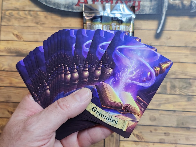 May include: A hand fans a deck of fantasy-themed cards with a purple and gold color scheme. The cards feature illustrations of books, potions, and magical effects. The word "Grimoire" is visible on one card.