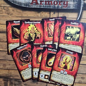 May include: A collection of fantasy-themed game cards with red and orange flames. The cards feature illustrations and text, including "Wyldfire Pact" and "Courage". The cards are arranged on a wooden surface.