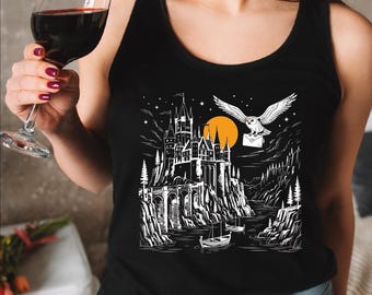 May include: Black tank top featuring a detailed black and white illustration of a castle, an owl carrying a letter, and a full moon. The design is reminiscent of a fantasy theme. A glass of red wine is held in the left hand.