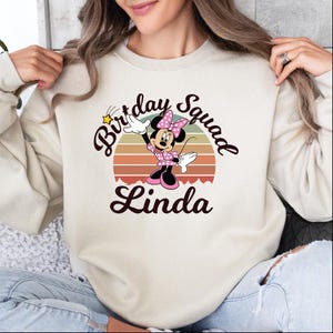 A woman wearing a white sweatshirt with a Minnie Mouse graphic and the text "Birthday Squad Linda" printed on it.