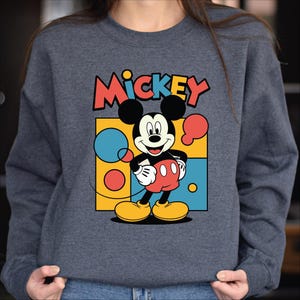A person wearing a gray sweatshirt with a colorful graphic of Mickey Mouse printed on it.