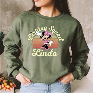 A woman wearing a green sweatshirt with a Minnie Mouse graphic and text that says "Birthday Squad Linda".