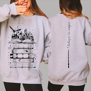 May include: A gray sweatshirt with a black and white graphic of Hogwarts castle, a stack of books, a flying snitch, and an owl. The back of the sweatshirt has a black and white graphic of a wand and the text "believe in magic".