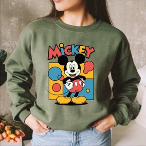 A woman wearing a green sweatshirt with a colorful graphic of Mickey Mouse printed on it.