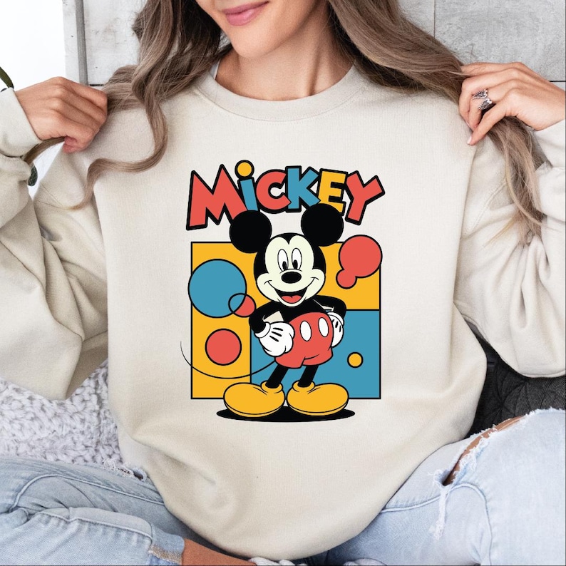 A woman wearing a white sweatshirt with a colorful graphic of Mickey Mouse printed on it.