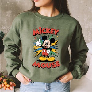 A woman wearing a green sweatshirt with a colorful graphic of Mickey Mouse.